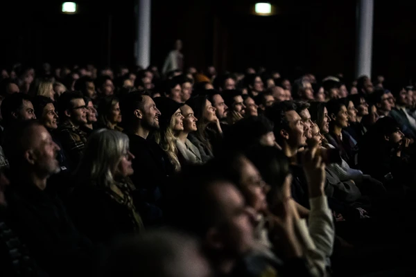 Audience at a Banff Tour event, lit by the glow of the screen, faces turned attentively toward the stage.