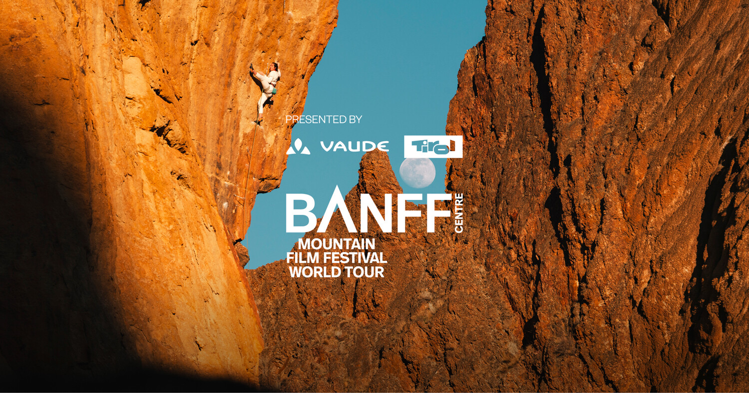 Banff Tour 2027 &ndash; Climber on a steep, overhanging rock face glowing orange, with a full moon rising over jagged rock spires against a blue sky in the background.