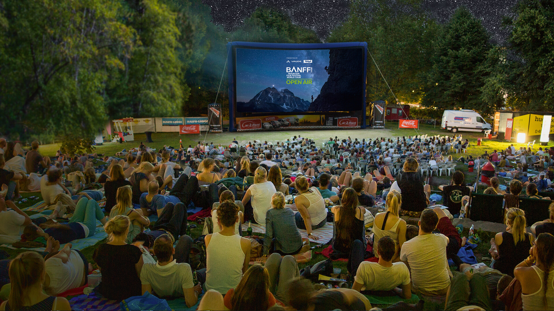 Open-air audience on a lawn in front of an inflatable Banff Tour screen during a screening under a starry sky.