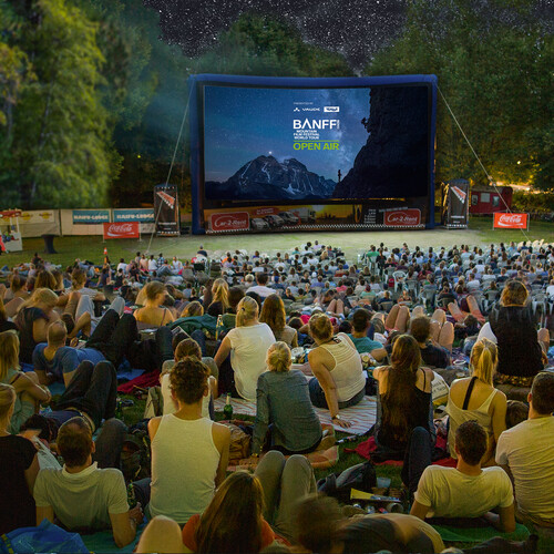 Open-air audience on a lawn in front of an inflatable Banff Tour screen during a screening under a starry sky.